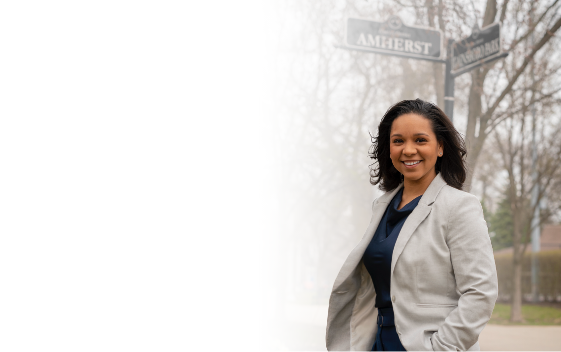 Amanda Treppa for State Senate campaign photo.  Blue large logo of Amanda Treppa for State Senate on the left and to the right is Amanda Treppa standing in front of her community Amherst street sign